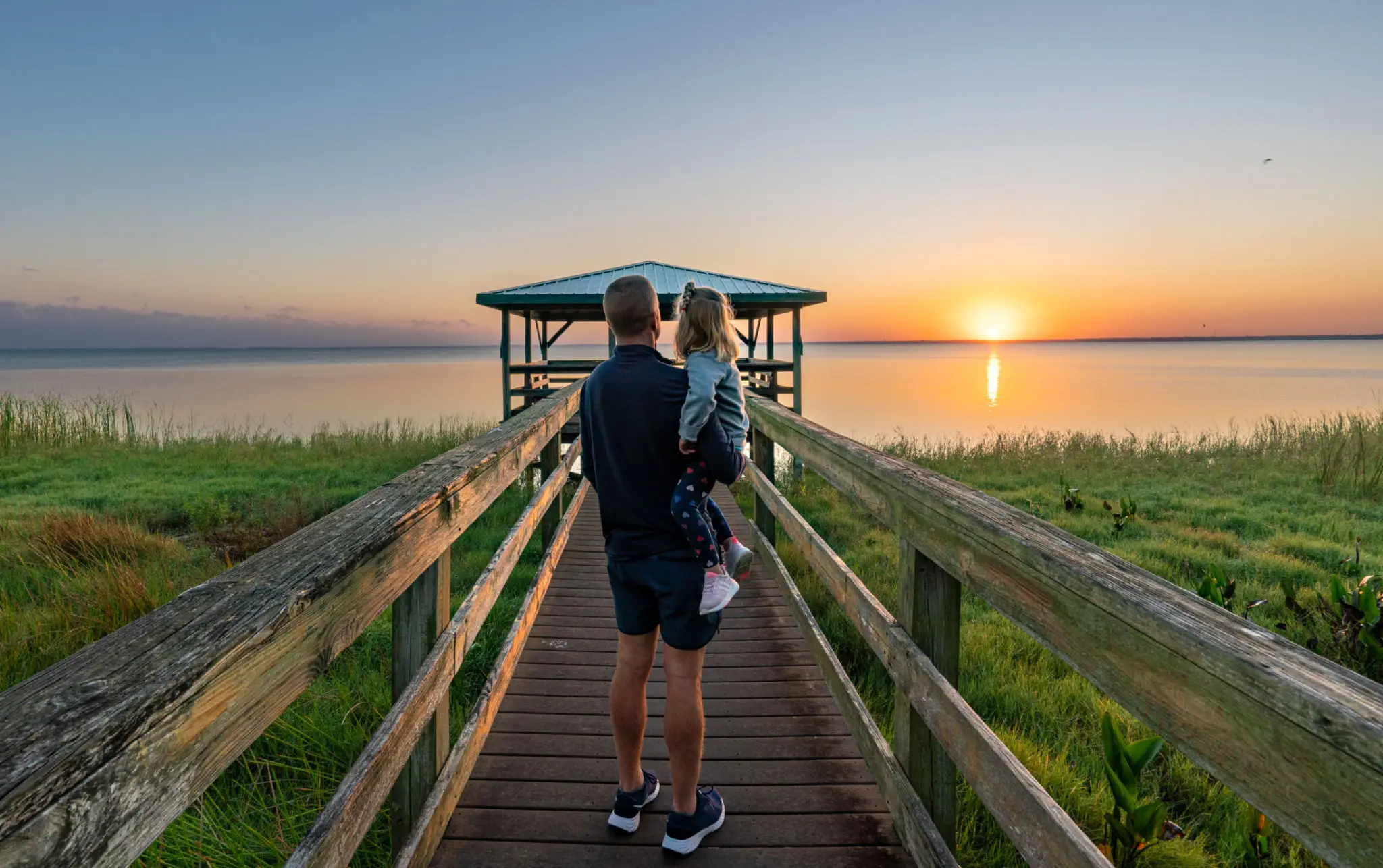 Father holding child on pier at sunrise